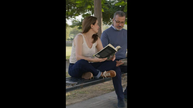 A mature couple reading sitting at the park bench share a gentle smile