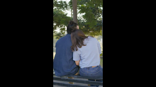 A young couple share a tender kiss and hub on a park bench on a sunny day